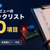 赤いチェックが入ったチェックリストの紙とクリップボード、赤ペン、光る赤いLEDとリレーが載った小さな基板の写真に、回路図レビューのチェックリスト20項目の文字